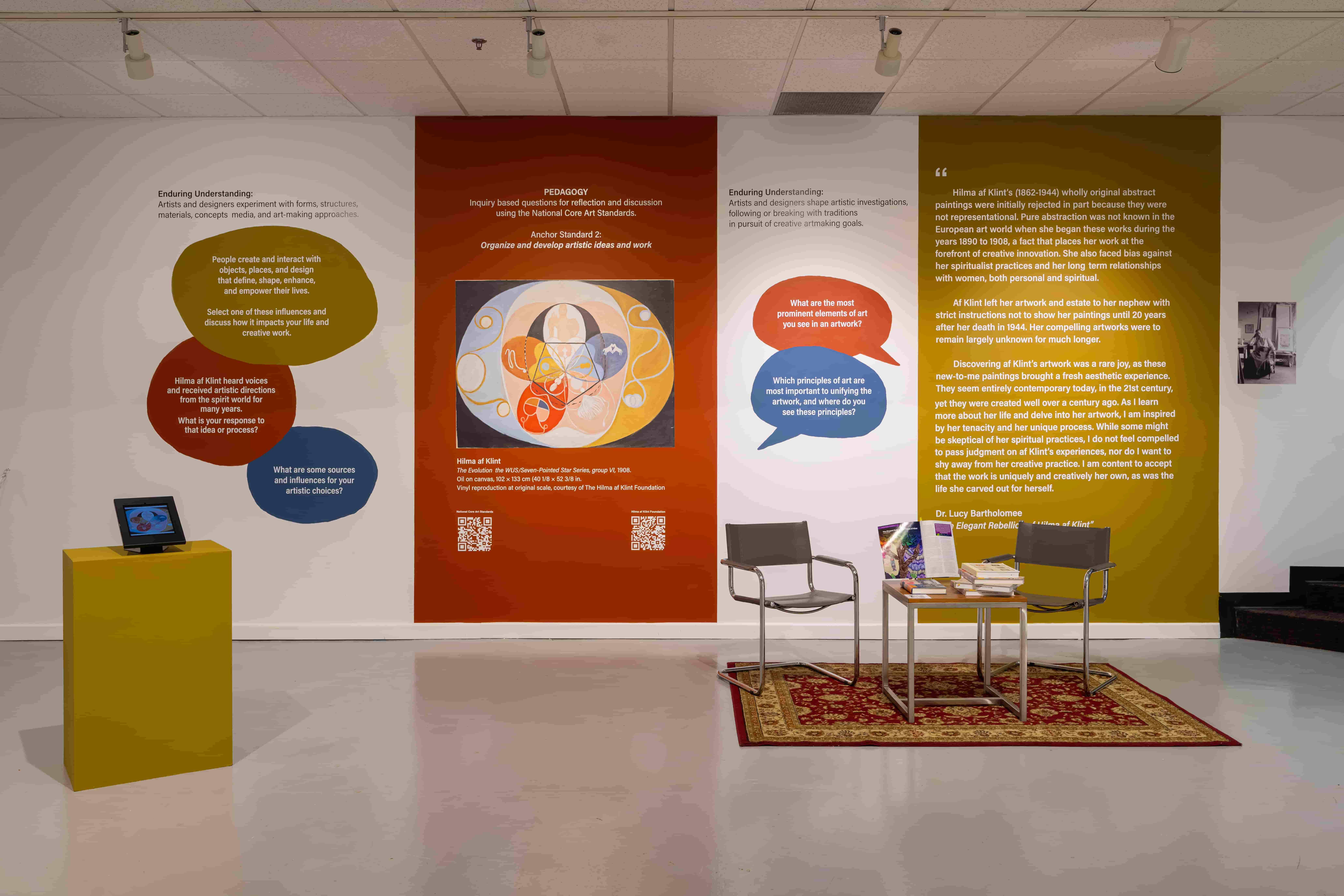 Museum wall display about artist Hilma af Klint, featuring educational text, discussion questions, a central painting reproduction, and a small pedestal with a digital screen.