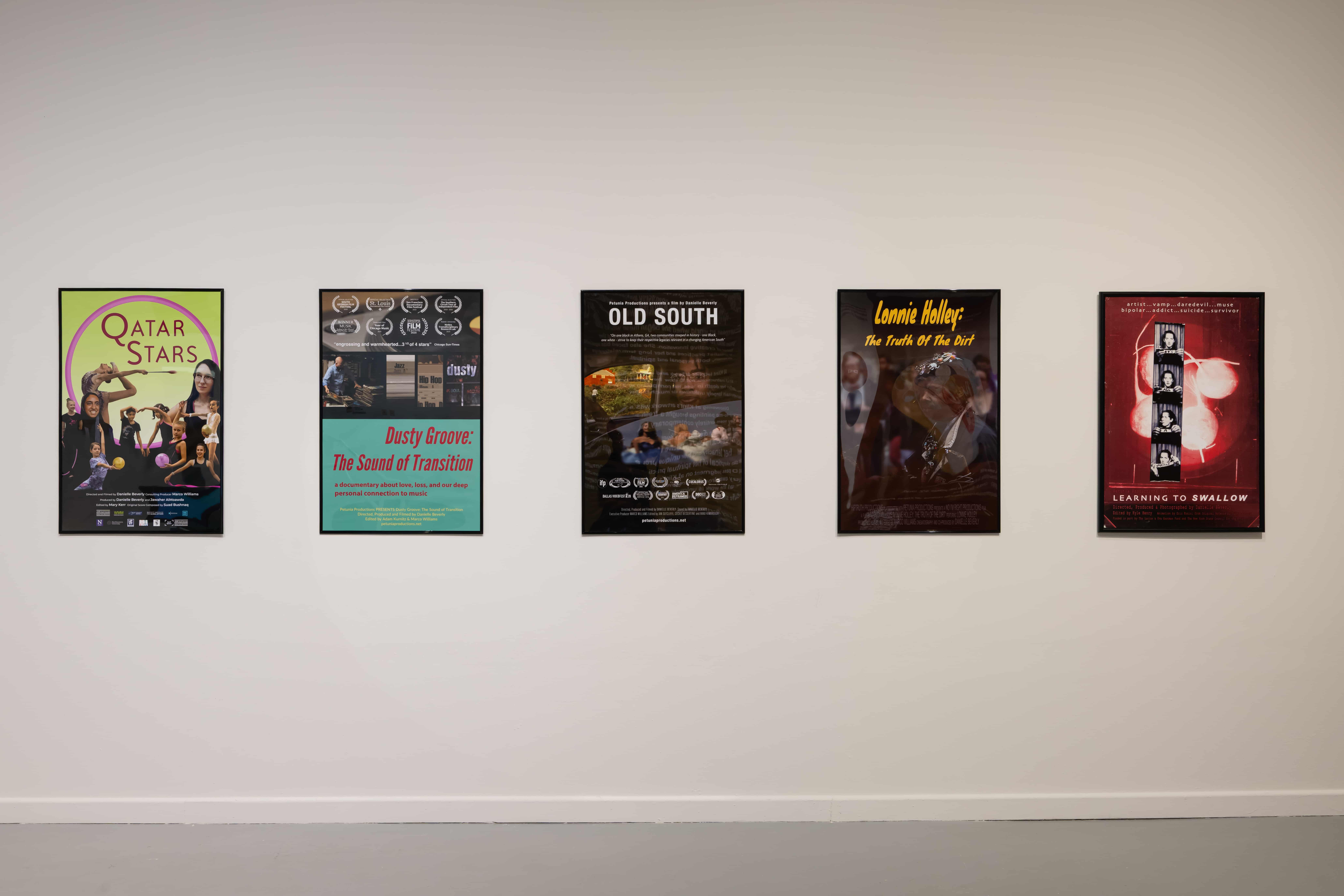 Five colorful music posters line a plain gallery wall: Qatar Stars, a tribute, Old South, a country music act, and a red album poster, creating a nostalgic concert mood.