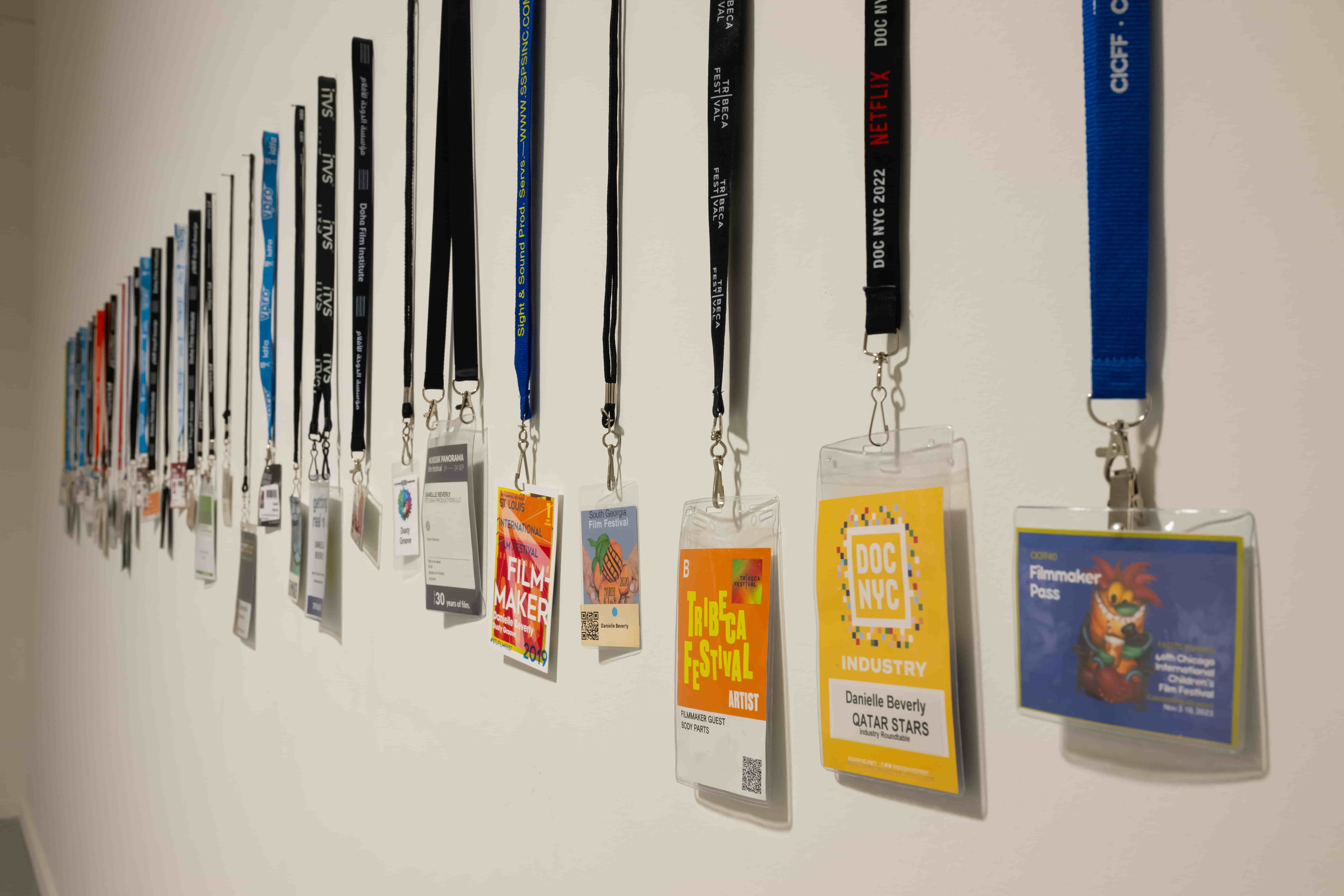 Colorful conference badges on assorted lanyards hang along a white wall, receding into the distance and suggesting a lively professional event.