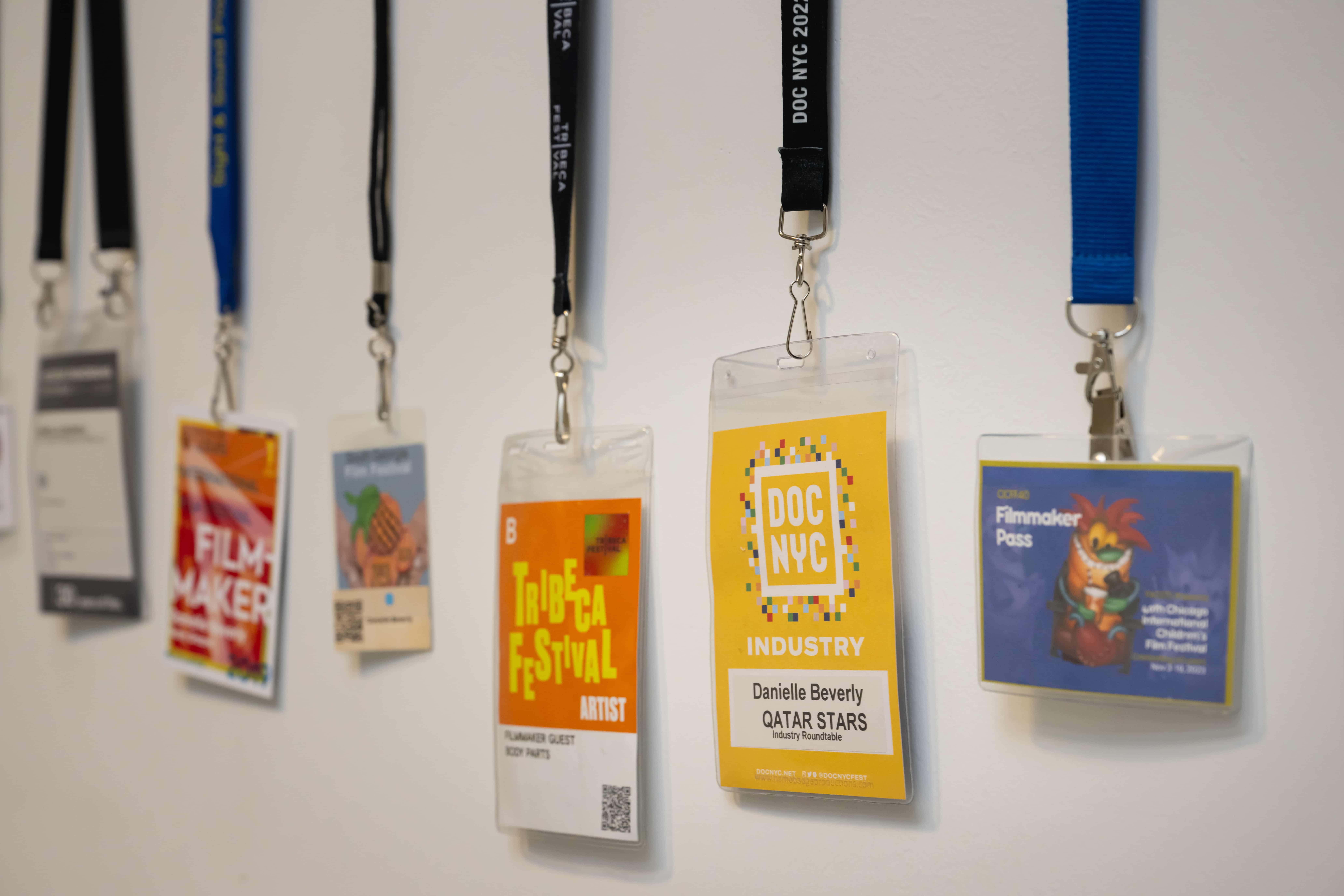 Colorful conference badges on assorted lanyards hang along a white wall, receding into the distance and suggesting a lively professional event.